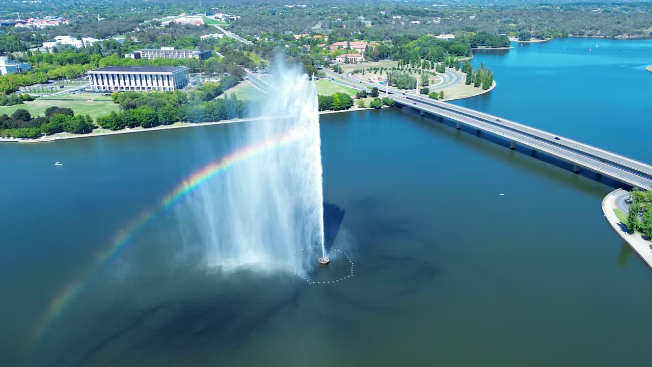 Drone aerial landscape of rainbow reflection within water fountain jets Captain Cook Memorial landmark with bridge overpass in Lake Burley Griffin Canberra ACT Australia travel tourism attraction