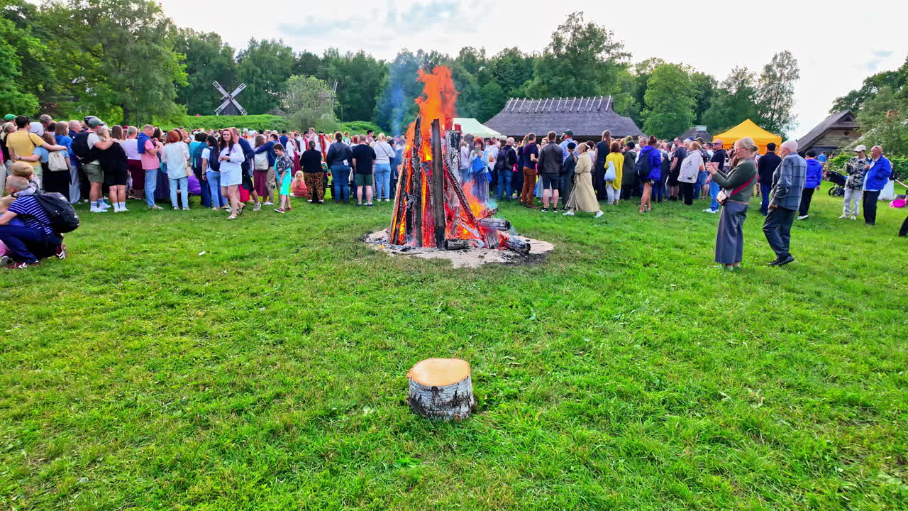 Large crowd gathered around a towering bonfire in an outdoor setting