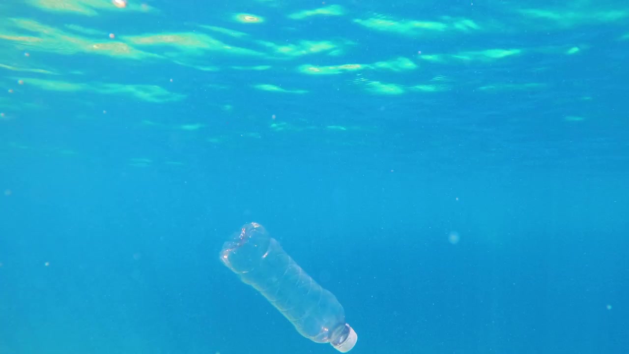 Bottiglia di plastica si muove nell'acqua marina. L'acqua è limpida e la luce del sole attraversa la superficie. L'inquinamento colpisce gli ecosistemi marini.