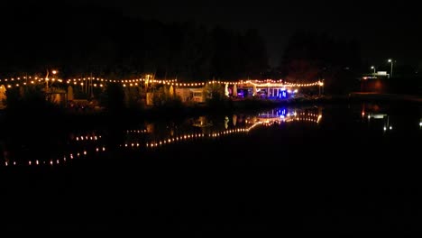 three pounds in katowice city - lakeside bar with shimmering lights reflections in water during nightime - aerial 4k