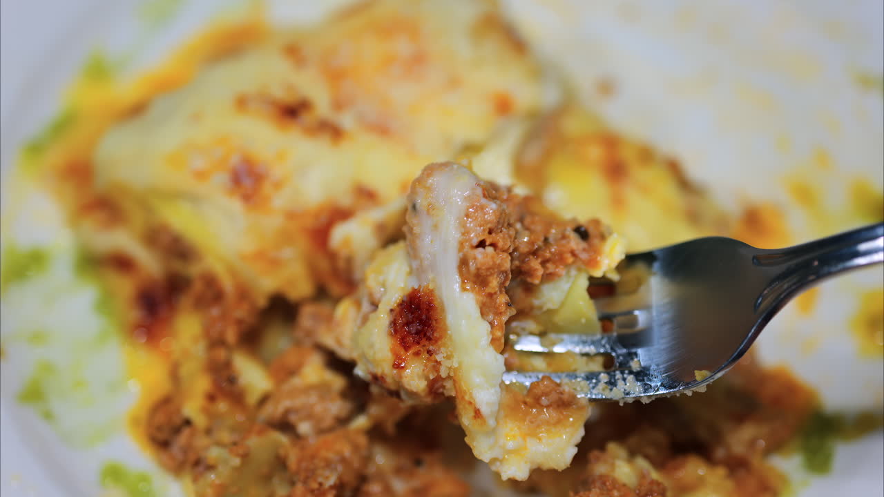 Close up of a fork picking up lasagna from a white plate