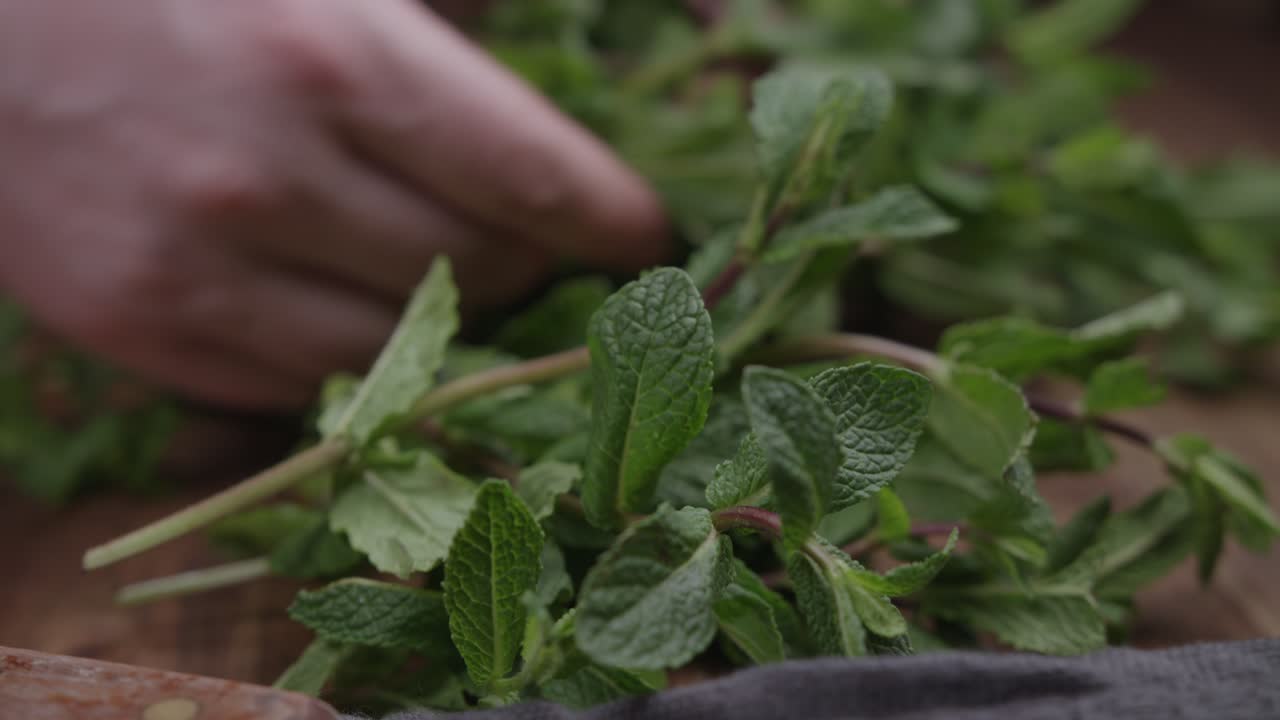 primer plano deslizante de un hombre eligiendo un poco de menta fresca en la cocina con un cuchillo cerca
