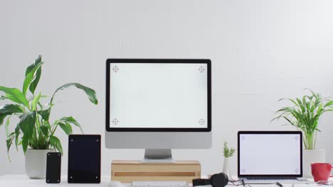 video of laptop, smartphone, tablet and computer on wooden table with copy space in office