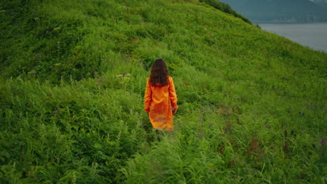 Woman in Orange Raincoat Hiking on a Hill