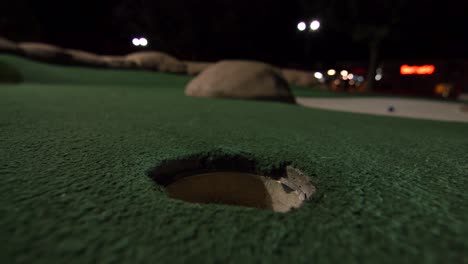 A-yellow-mini-golf-ball-falls-into-the-golf-hole-and-bounces-in-the-pocket-on-a-course