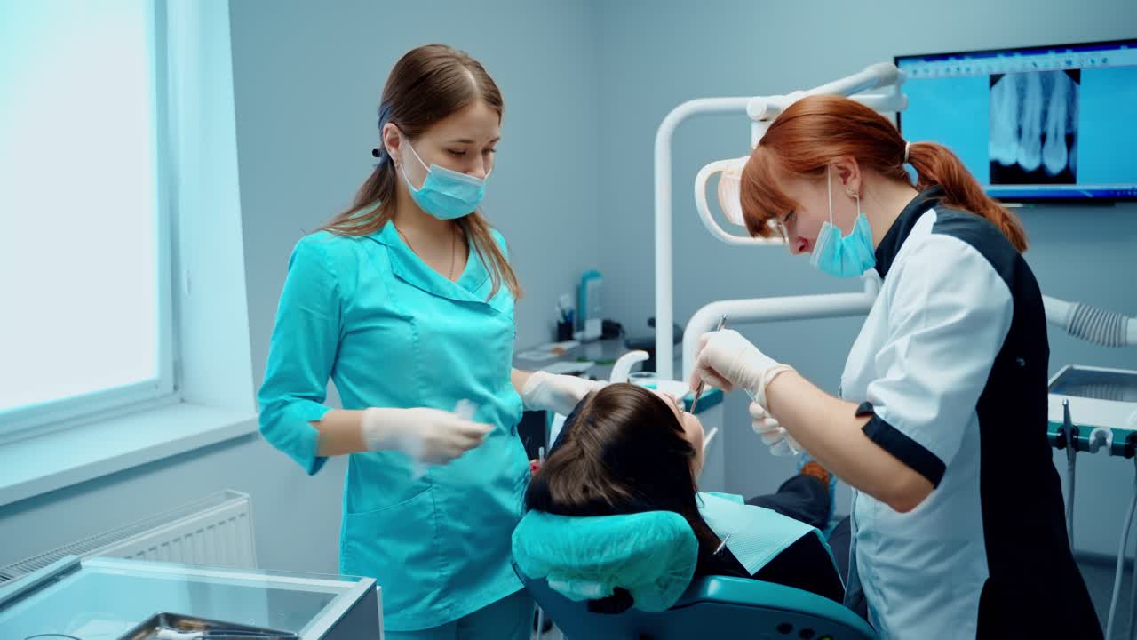 Patient at dentist's office. Female stomatologist together with assistant in medical uniform are treating woman's teeth in modern clinic.