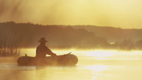 distant view of senior man in a hat sailing in a boat on the lake at sunset