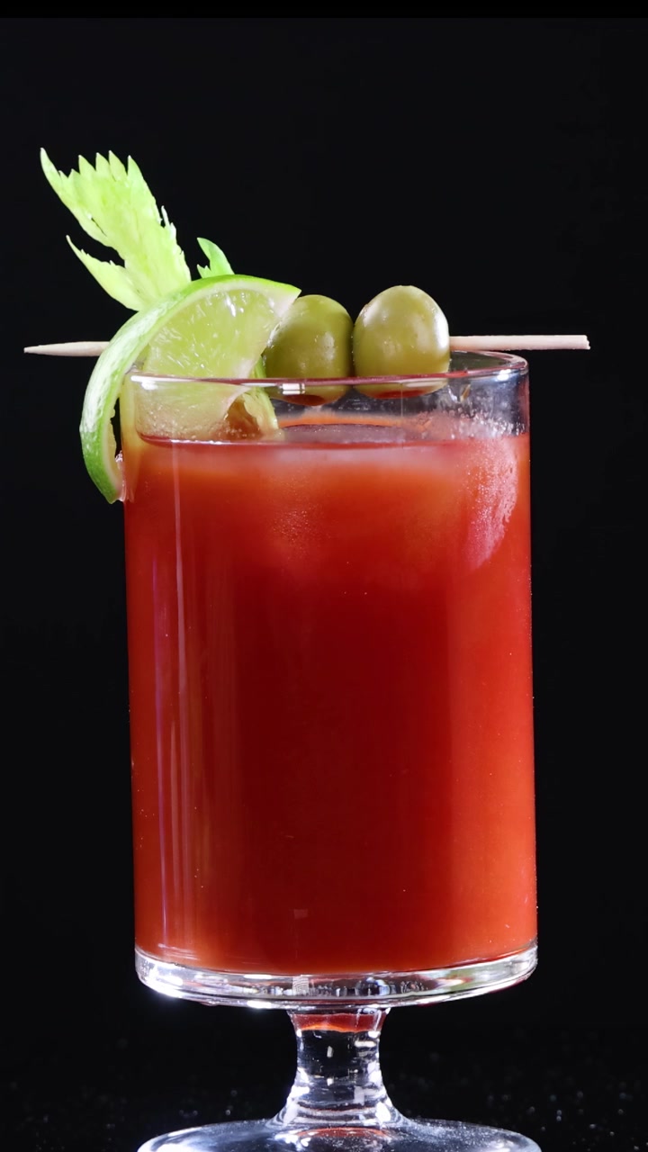 Um coquetel Bloody Mary é guarnecido com azeitonas, limão e aipo em um fundo preto.