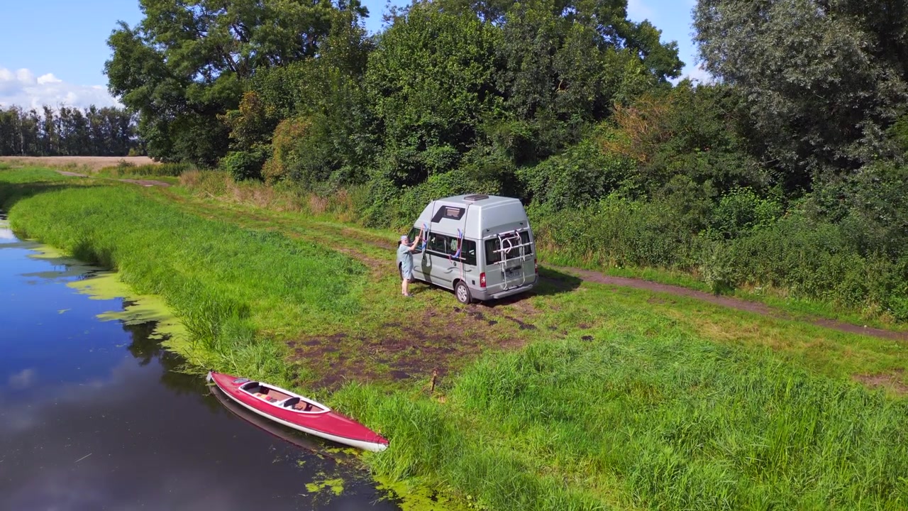 Uomo con pedalò rosso sulla riva. Perfetto volo aereo con vista dall'alto di caravan, campeggio e camper sul fiume, estate 2023, Germania, Havelland. Drone statico con treppiede in hovering, cinematico 4K.