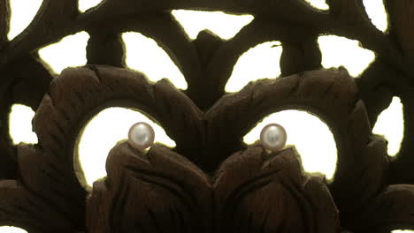 Two pearl earrings displayed on carving, static