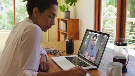 Mixed-race-businesswoman-sitting-at-desk-using-laptop-having-video-call-with-male-colleague