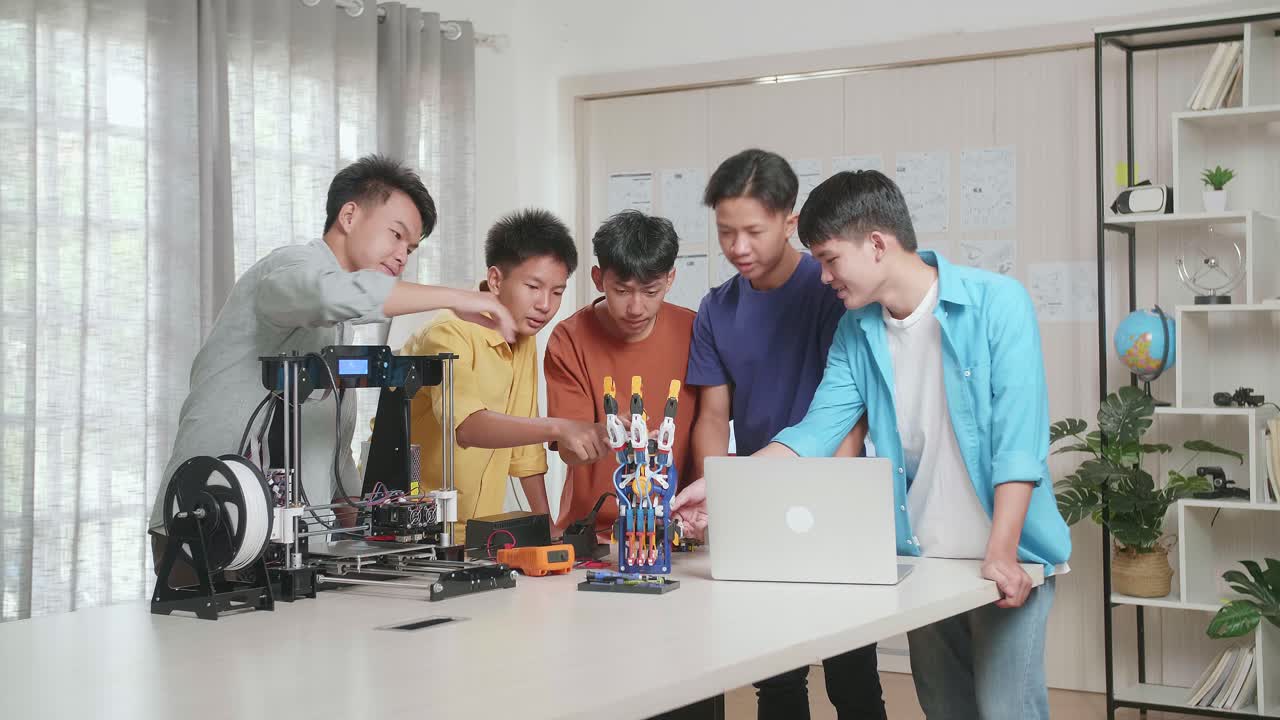 노트북과 3d 프린팅을 가진 젊은 아시아 소년 그룹이 집에서 사이보그 손에 대해 논의하는 동안 미소 짓고 카메라에 팔을 고 있습니다.