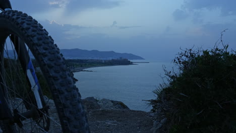 time lapse captures mountain bike parked near rocky sea coastline during sun rise over mountain range