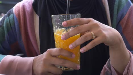 a woman in a hijab sitting at a table drinking orange juice