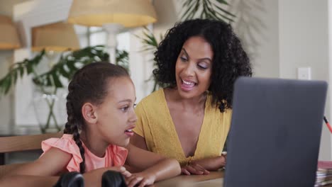 biracial girl with mother learning online using laptop at table, slow motion