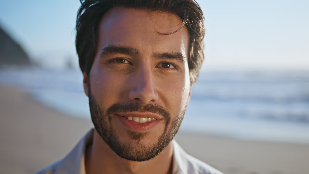 Primer plano de hombre hispano sonriendo de pie en una playa soleada. Retrato de hombre barbudo feliz