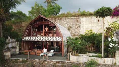 drone shot of a couple standing outside of they villa, enjoying the great luxury apartment. the villa is build from organic materials. lots of plants around it. togetherness and love while travelling