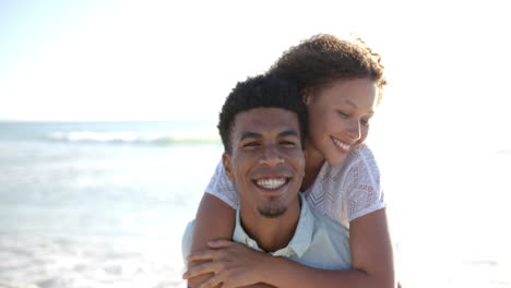 Una-Pareja-Birracial-Se-Abraza-En-Una-Playa-Soleada,-Con-Los-Brazos-De-La-Mujer-Alrededor-De-Los-Hombros-Del-Hombre.