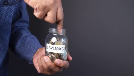 young man saving coins in a jar on black background