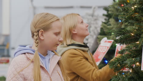 Mom-and-daughter-choose-a-Christmas-tree-in-the-supermarket.-Holiday-shopping