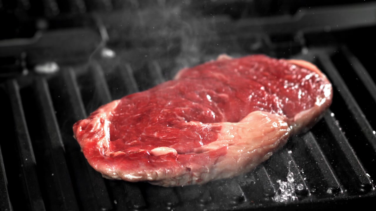 Raw Steak Sizzling and Steaming on a Hot Grill