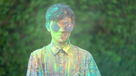 portrait of boy standing being covered in coloured powder at holi festival.