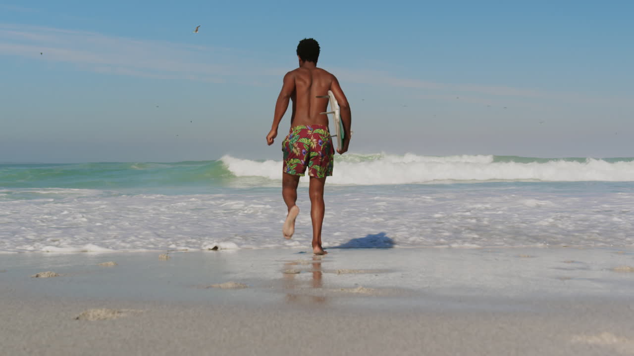 surfista masculino corriendo hacia el mar en la playa 4k