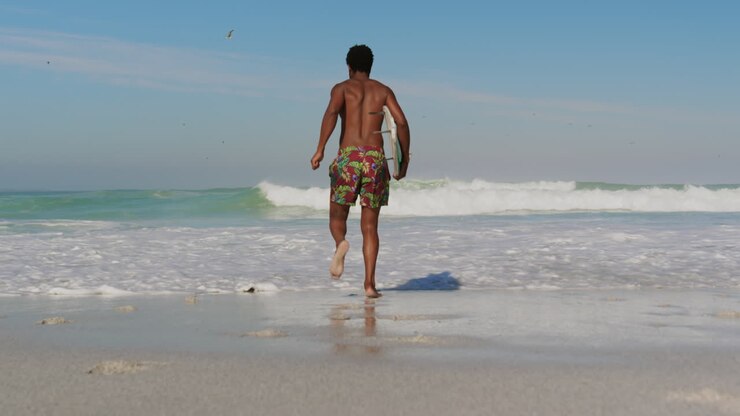 Male surfer running towards sea at beach 4k