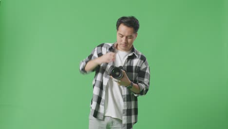 asian photographer changing lens of camera before using it taking pictures while standing on green screen background in the studio