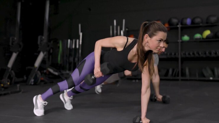 Donna e uomo che eseguono renegade rows con manubri in una palestra moderna