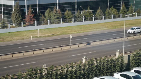 top view of divided highway with cars passing on double carriageways near buildings at daytime in slowmo