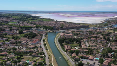 Boat-in-a-canal-along-Aigues-Mortes-medieval-city-aerial-pink-ponds-full-of-salt