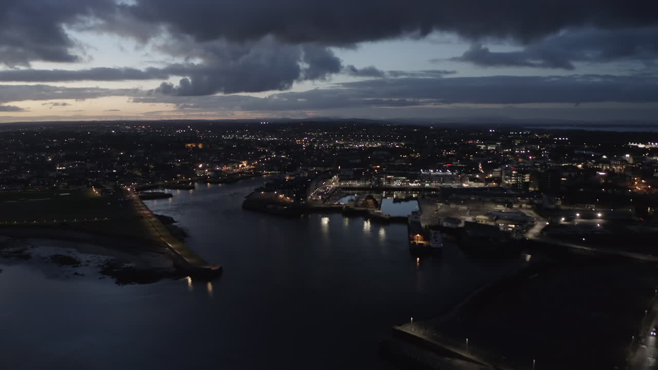 Aerial dolly capturing Galway city at twilight, city lights glowing under dramatic sky