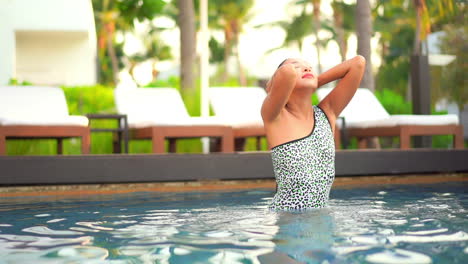 una bella mujer emerge de una piscina y se quita el pelo mojado