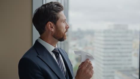 worker looking paper airplane standing at window closeup. man thinking on rest.