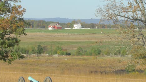 wide-open view of the battlefield of gettysburg with a cannon in first term and a red barn on the horizon