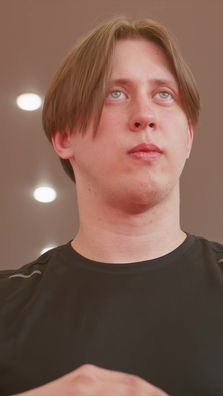 Close up of young man with light brown hair wearing. His head and upper body remain mostly still as man manipulates. Background is plain or softly lit indoor environment