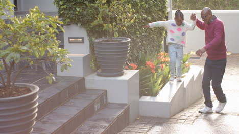 african american grandfather with granddaughter jumping in sunny garden, copy space, slow motion