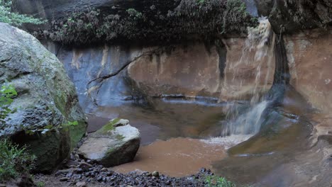 Brown-flood-water-forms-small-waterfall-in-Liphofung-canyon,-Lesotho