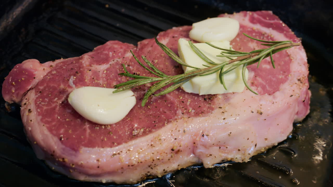 Primo piano di una bistecca che cuoce su una piastra grill guarnita con rosmarino fresco.