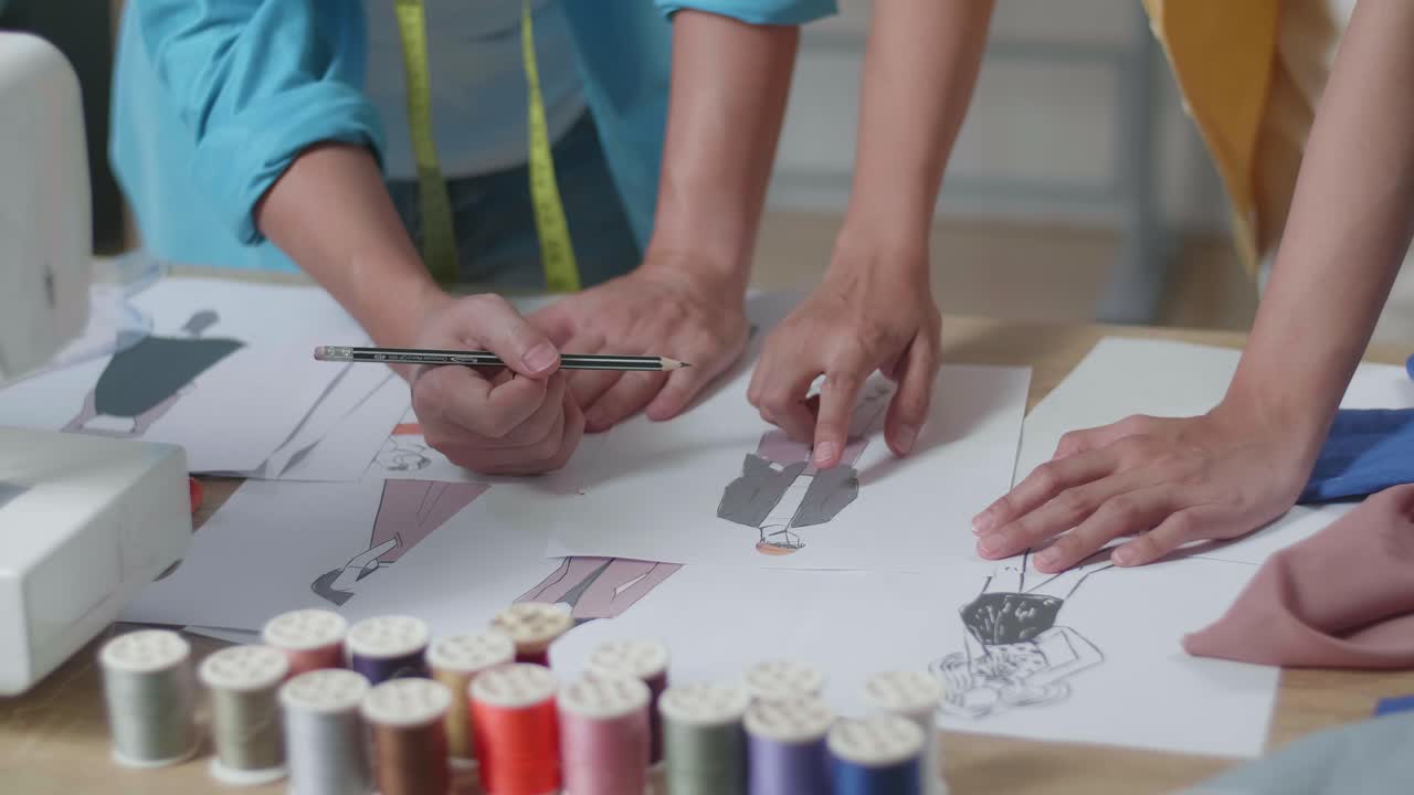 남자와 여자 디자이너의 손이 스튜디오에서 종이에 옷을 디자인하는 클로즈업