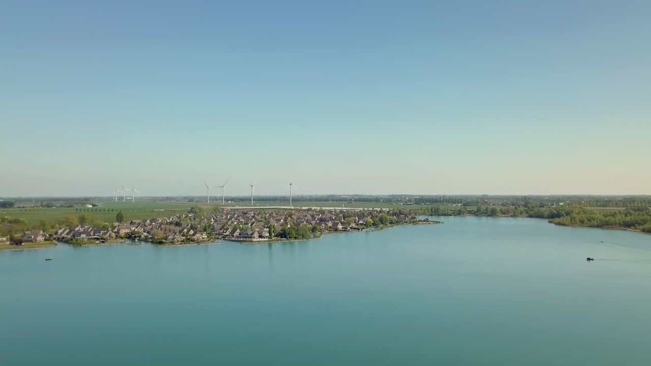 Aerial drone shot of flying up at the lake revealing the suburban and flat landscape with the wind turbines in the Netherlands.