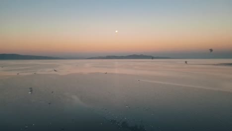 Seagulls-soar-through-hazey-yellow-orange-sky-above-Great-Salt-Lake,-Antelope-Island-in-background