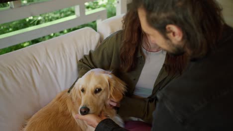 ein mann und ein brünettes mädchen streicheln einen hellfarbenen hund in einem pavillon in der natur. ein mädchen in einer grünen jacke und ein hellfarbener hund interagieren in einem pavillon in der natur