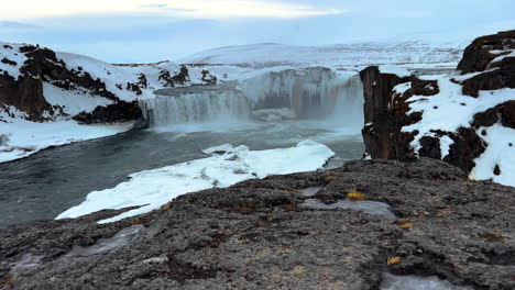 Zeitlupenaufnahme-Des-Goðafoss-Wasserfalls,-Umgeben-Von-Schneebedeckten-Hügeln-Auf-Island-Während-Des-Tages