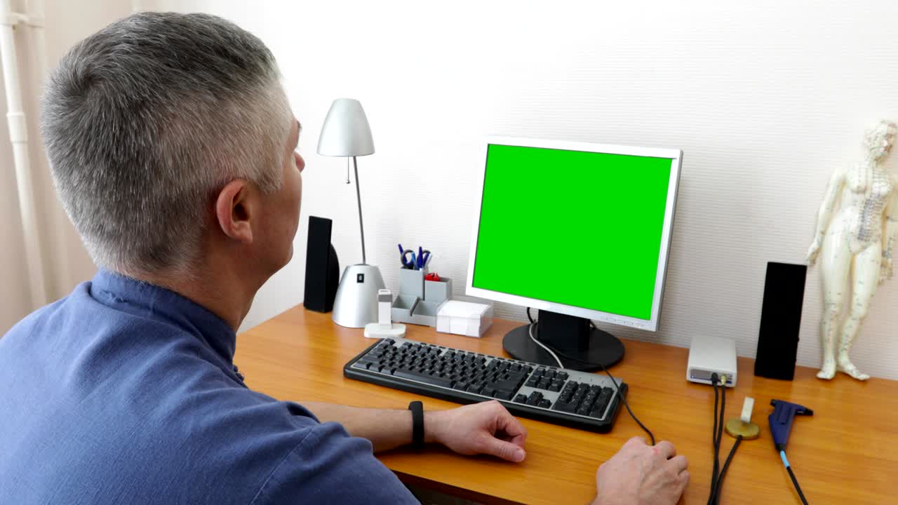 doctor sits at the computer with a green screen