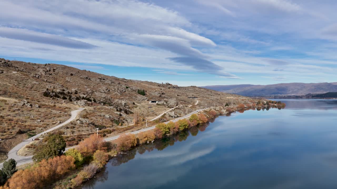 Drone footage captures serene Lake Dunstan with surrounding hills and clear skies in Cromwell, New Zealand. Smooth camera movement enhances tranquility