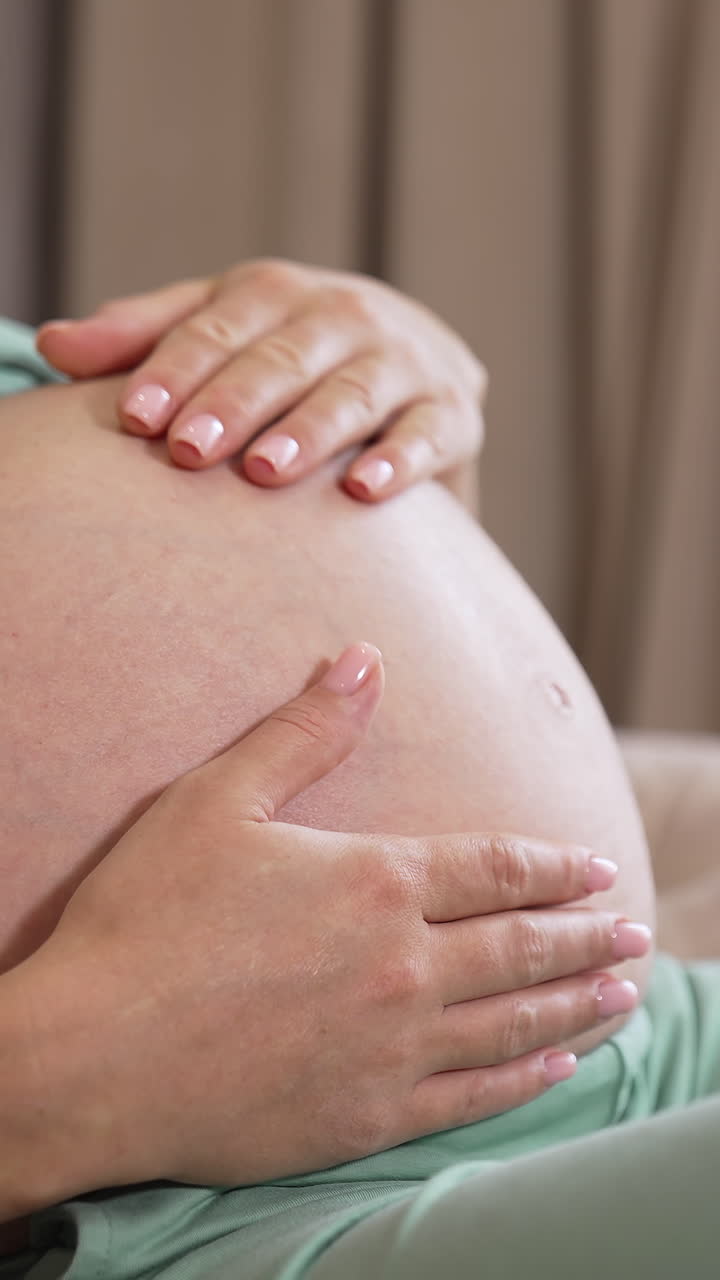 Donna incinta accarezza il pancione. Primo piano di donna incinta felice con il pancione a casa.