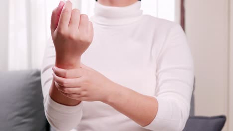 소파에 앉아 마사지를 하고 손목을 꽉 쥐고 긴장을 풀고 통증을 완화하는 여성