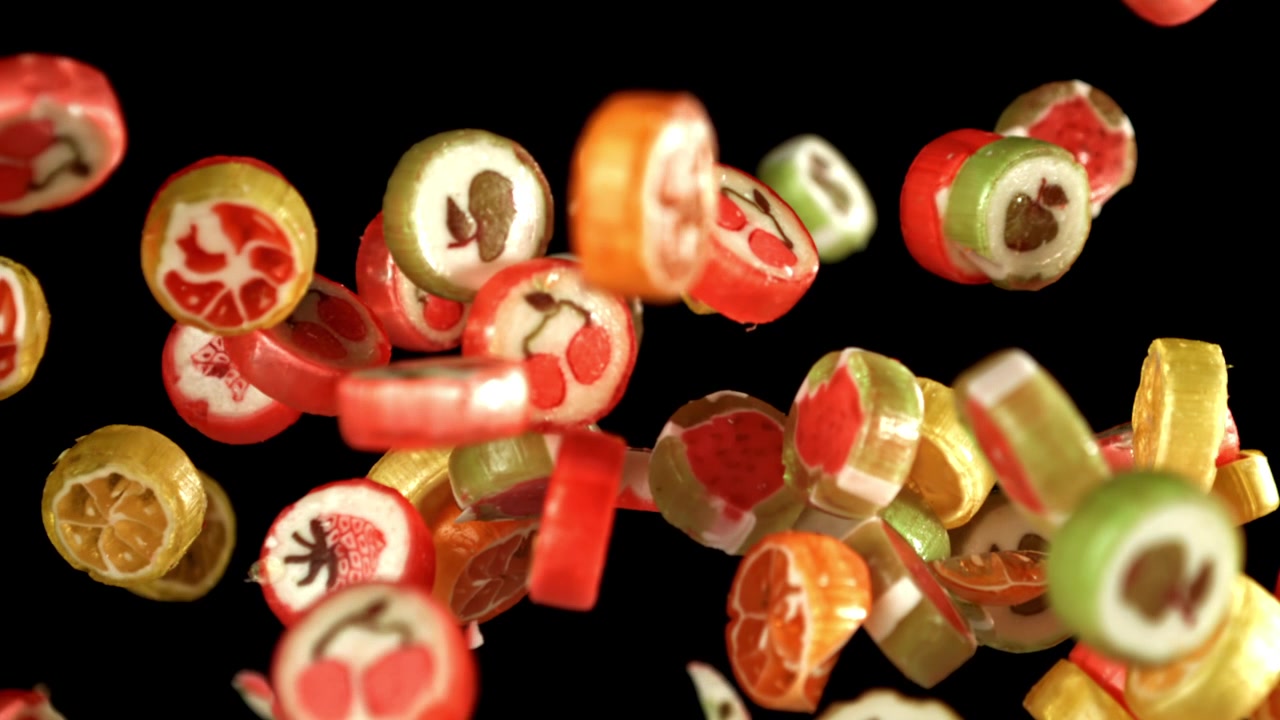 Bunte Fruchtbonbons fallen in Zeitlupe vor schwarzem Hintergrund